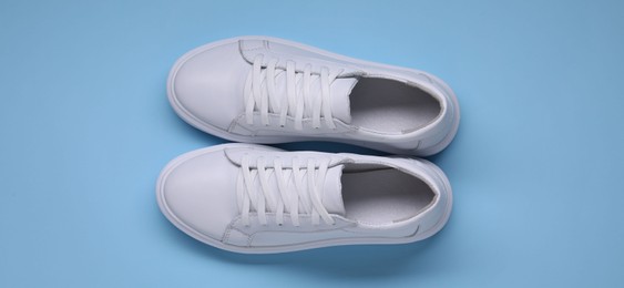 Photo of Pair of stylish white sneakers on light blue background, top view