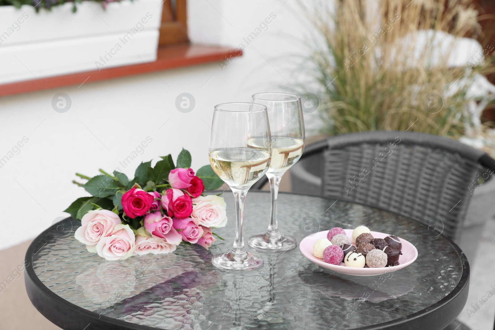 Photo of Bouquet of roses, glasses with wine and candies on glass table on outdoor terrace