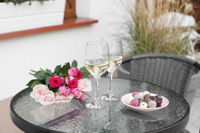 Photo of Bouquetroses, glasses with wine and candies on glass table on outdoor terrace
