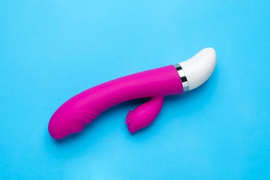 Photo of Pink vaginal vibrator on light blue background, top view. Sex toy