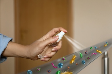 Image of Woman spraying antiseptic onto metal railing full of microbes indoors, closeup