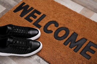 Photo of New clean mat with word WELCOME and shoes on floor