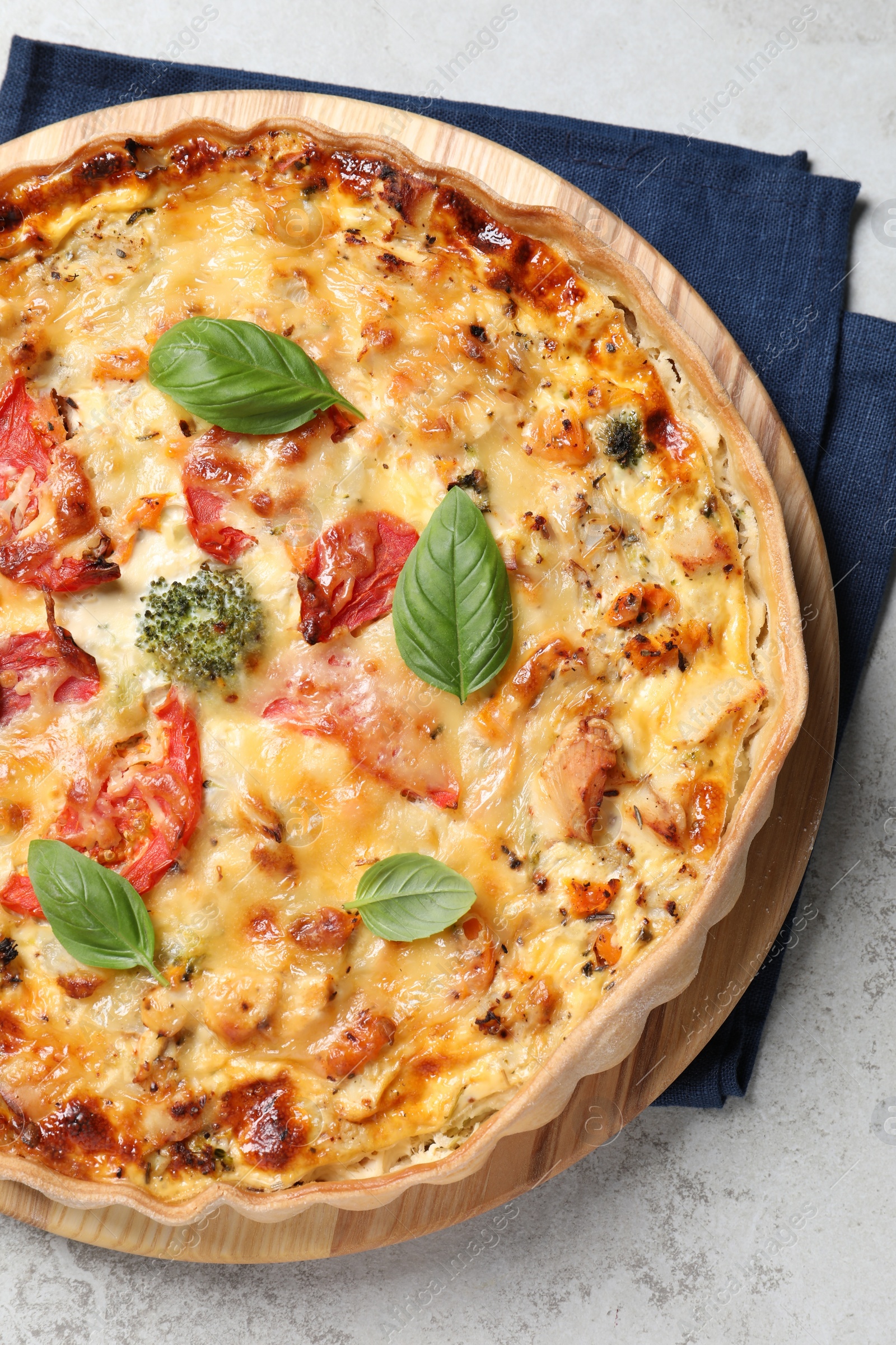 Photo of Tasty quiche with cheese, tomatoes and basil leaves on light grey table, top view.