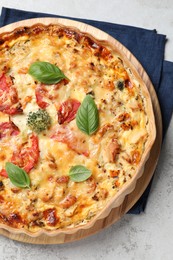 Tasty quiche with cheese, tomatoes and basil leaves on light grey table, top view.