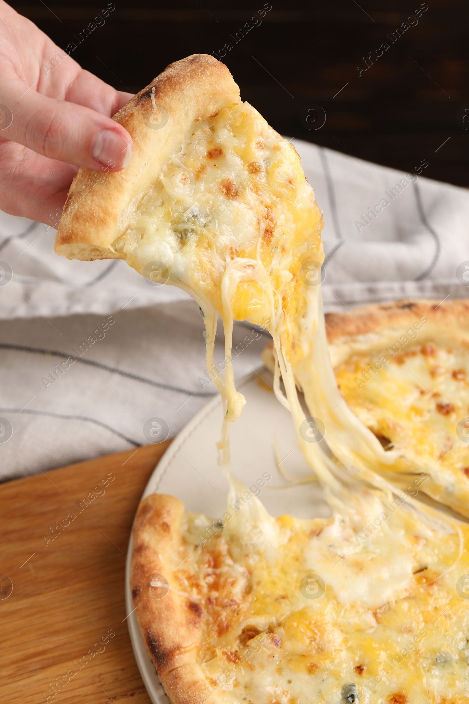 Photo of Woman taking piece of delicious cheese pizza at table, closeup