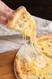 Photo of Woman taking piece of delicious cheese pizza at table, closeup