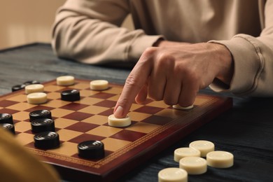Photo of Playing checkers. Man thinking about next move at wooden table, closeup