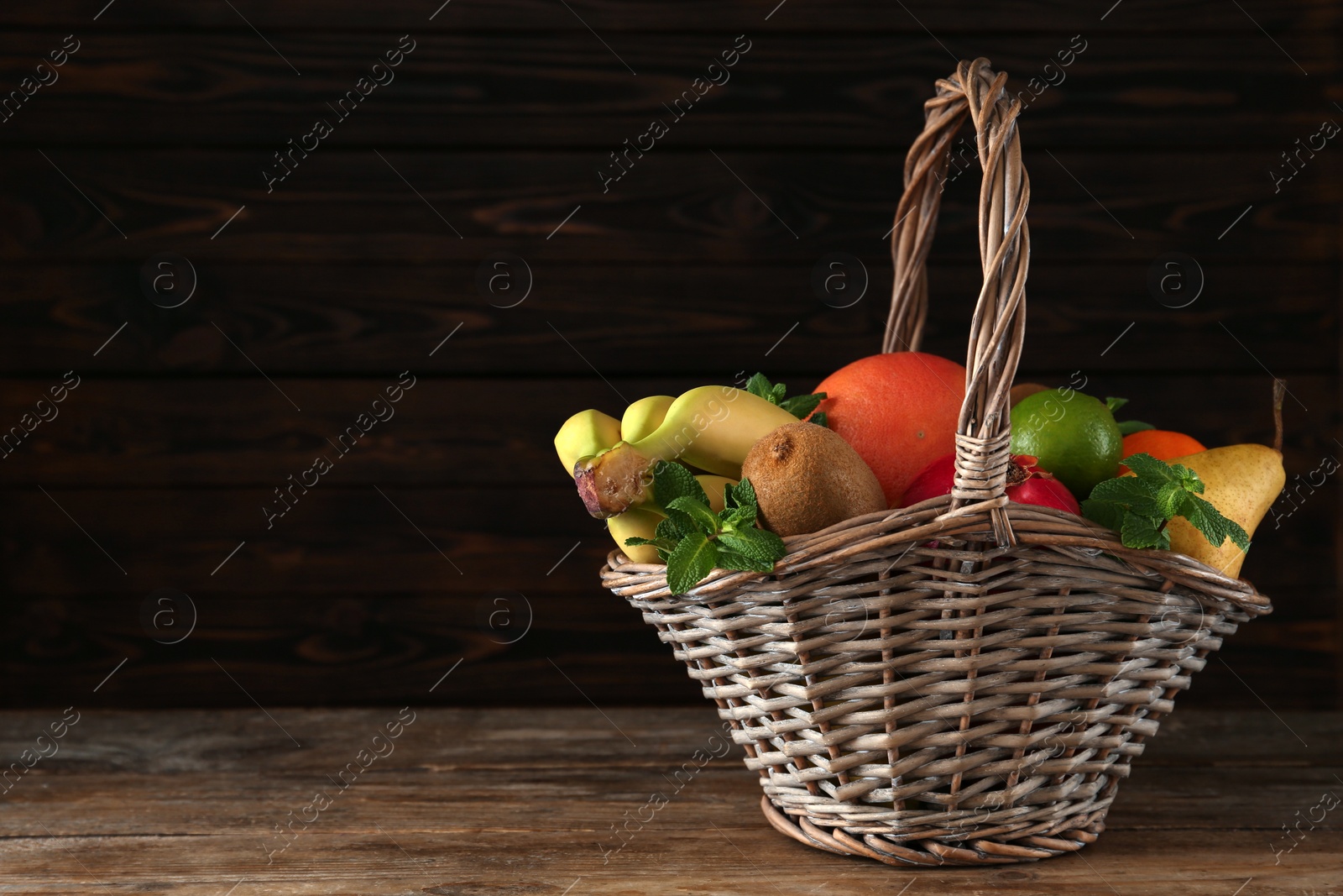 Photo of Wicker basket with different ripe fruits on wooden table. Space for text