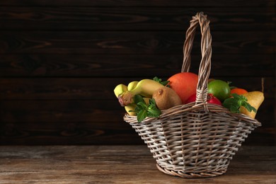 Wicker basket with different ripe fruits on wooden table. Space for text