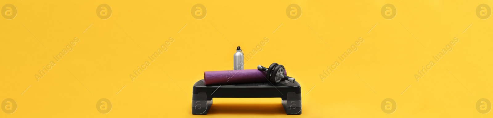 Image of Step platform, mat, bottle of water and abdominal wheel on yellow background. Banner design