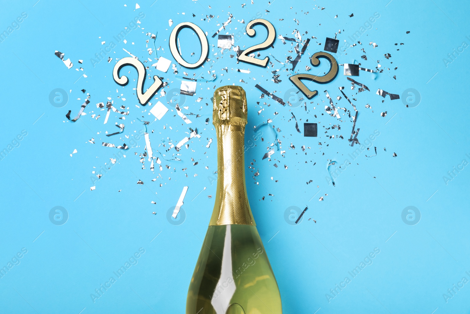 Photo of Bottle of sparkling wine, shiny confetti and number 2022 on light blue background, flat lay. Happy New Year