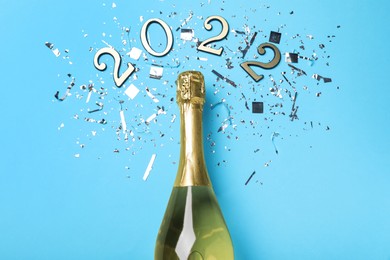 Bottle of sparkling wine, shiny confetti and number 2022 on light blue background, flat lay. Happy New Year