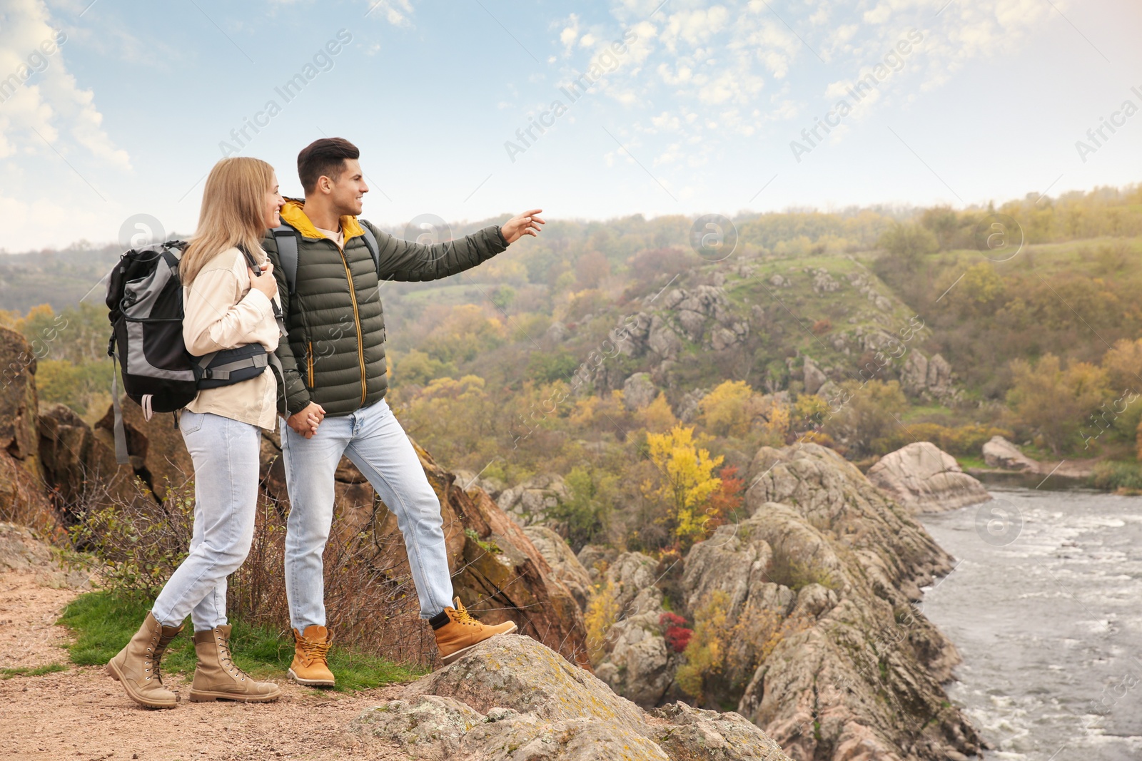 Photo of Couple of travelers with backpacks enjoying beautiful view near mountain river. Autumn vacation