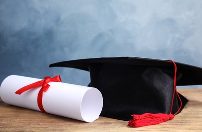 Photo of Graduation hat and student's diploma on wooden table against light blue background