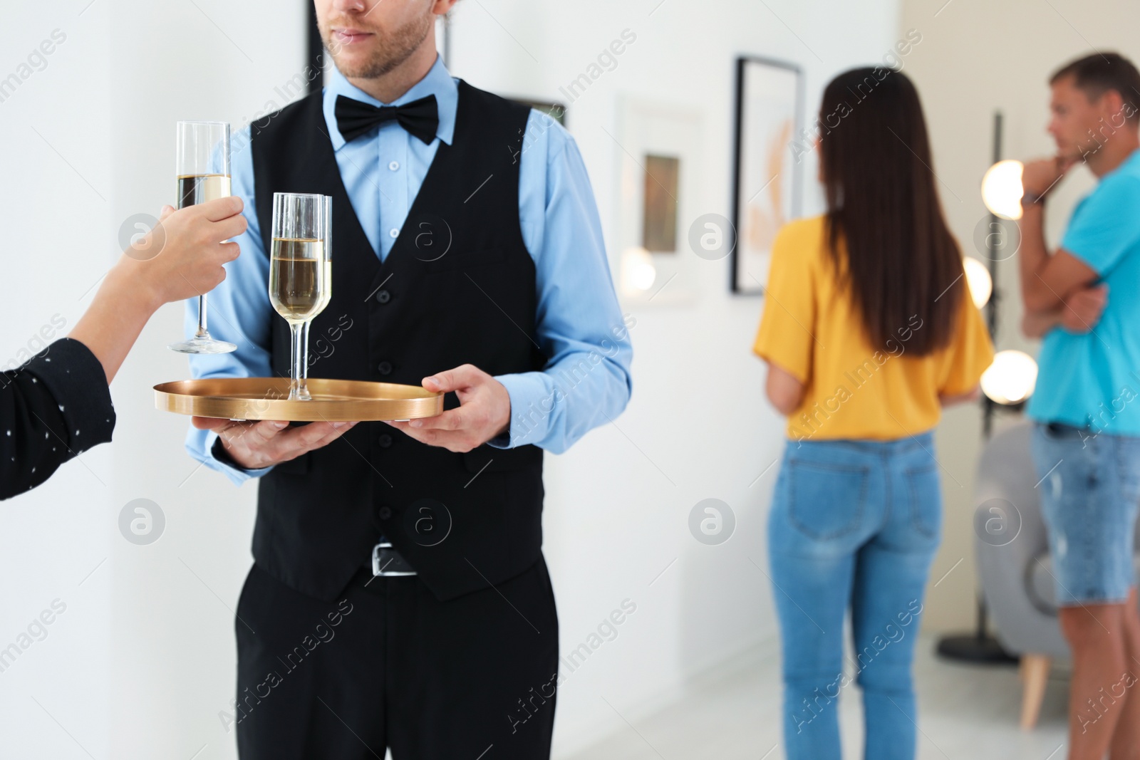 Photo of Waiter serving champagne to woman at exhibition in art gallery