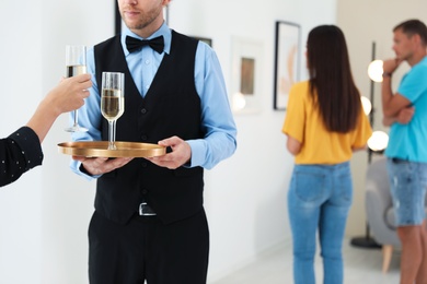 Waiter serving champagne to woman at exhibition in art gallery