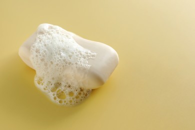 Photo of Soap bar with fluffy foam on yellow background, space for text