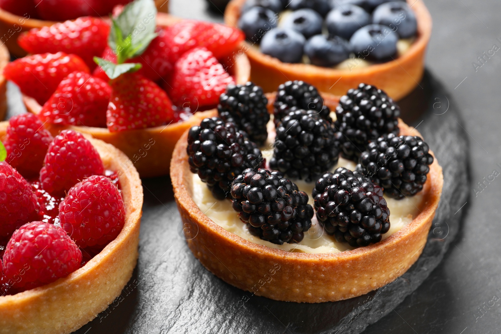 Photo of Tartlets with different fresh berries on table, closeup. Delicious dessert