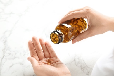 Woman with fish oil pills at table, closeup