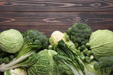 Photo of Many different types of fresh cabbage on wooden table, flat lay. Space for text