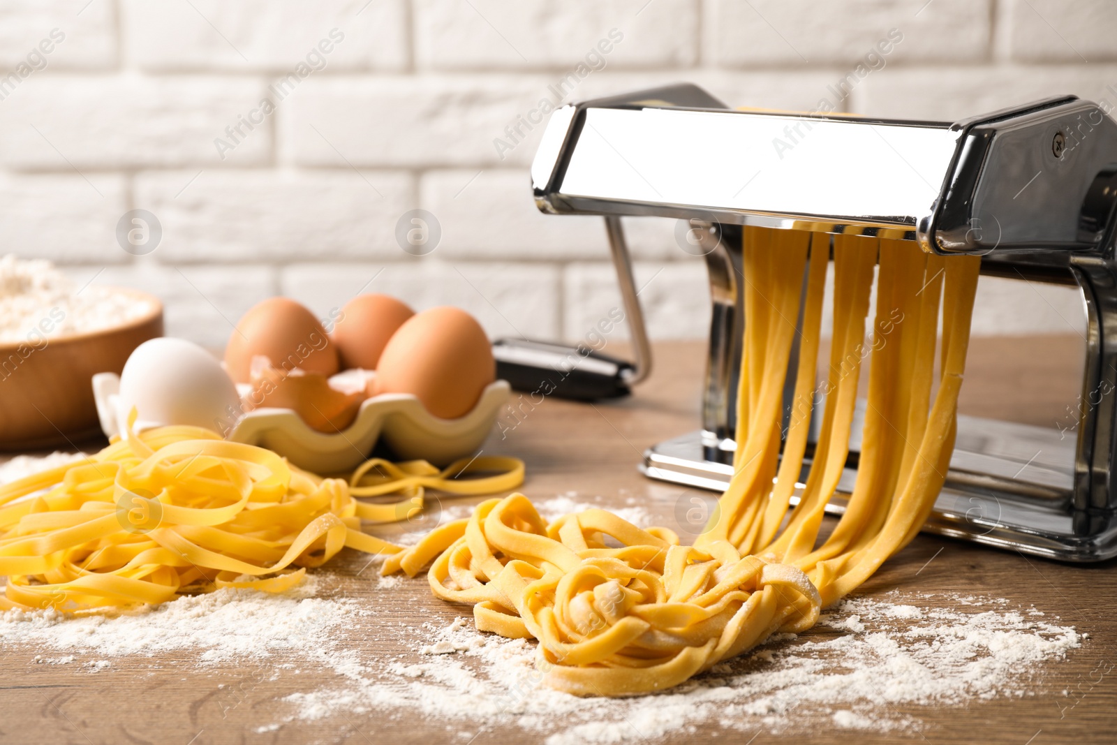 Photo of Pasta maker machine with dough and products on wooden table