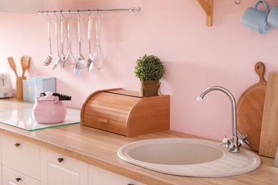Photo of Stylish kitchen with sink and clean dishware near pink wall