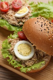 Photo of Delicious sandwiches with tuna, boiled egg and vegetables on wooden board