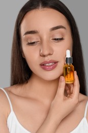 Beautiful young woman with essential oil on light grey background, closeup