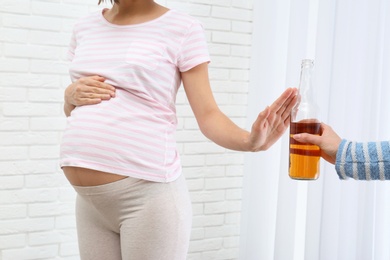 Photo of Pregnant woman declining whiskey indoors. Alcohol harm