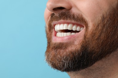 Happy man with healthy clean teeth on light blue background, closeup. Space for text