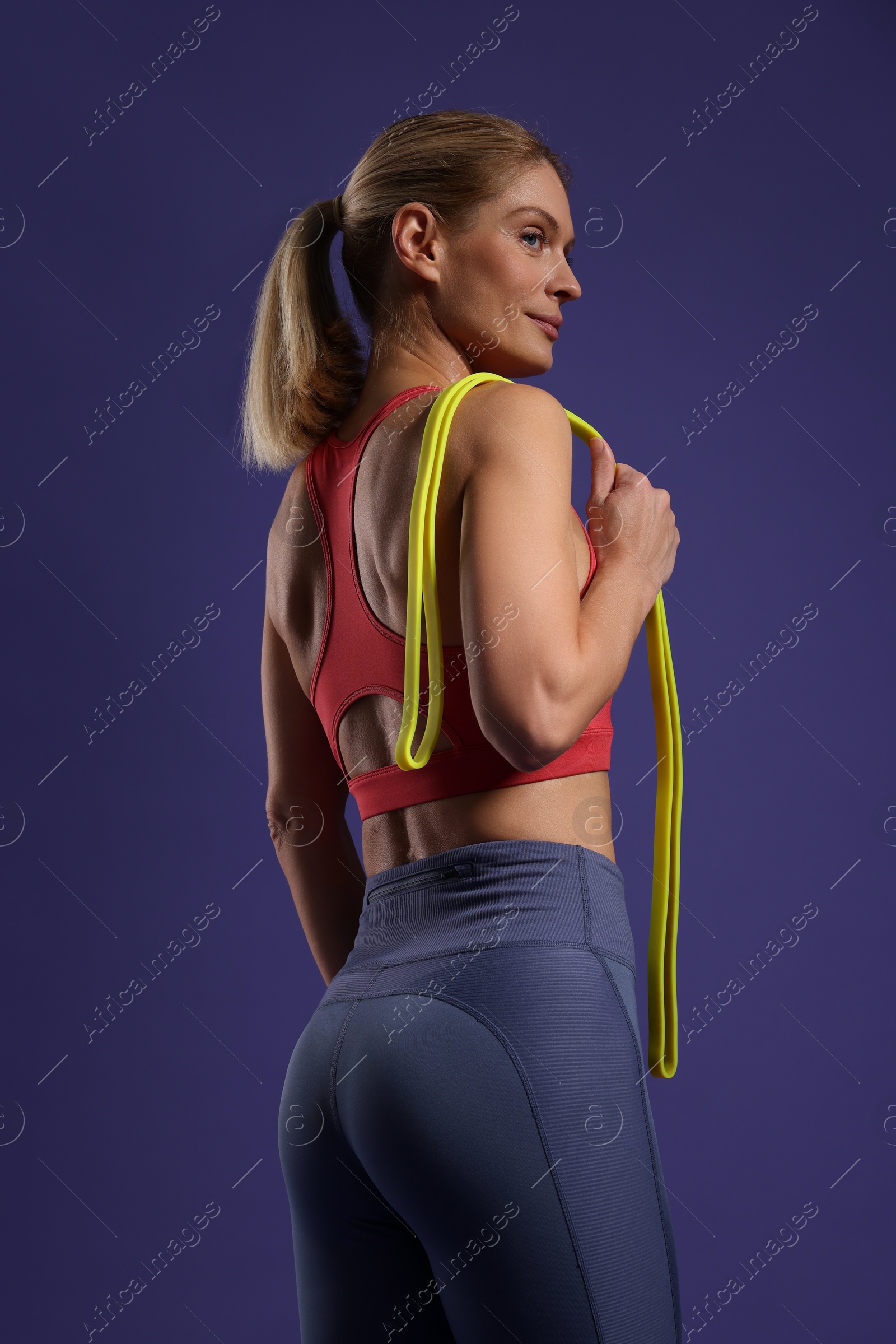 Photo of Beautiful woman with elastic resistance band on purple background, low angle view