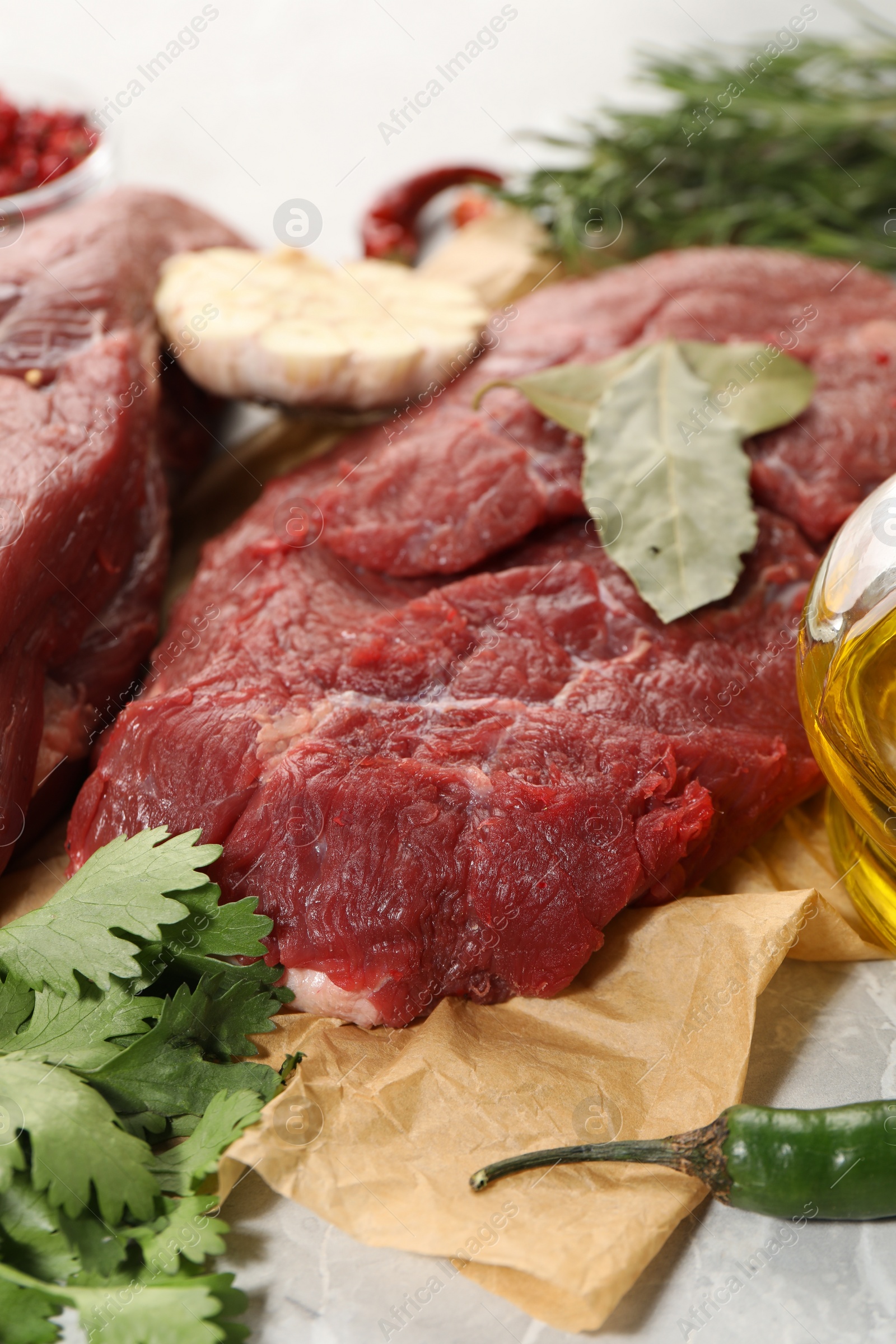 Photo of Pieces of raw beef meat, parsley and pepper on light grey table, closeup