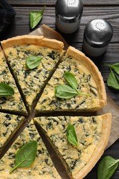 Photo of Sliced delicious homemade spinach pie on black wooden table, flat lay