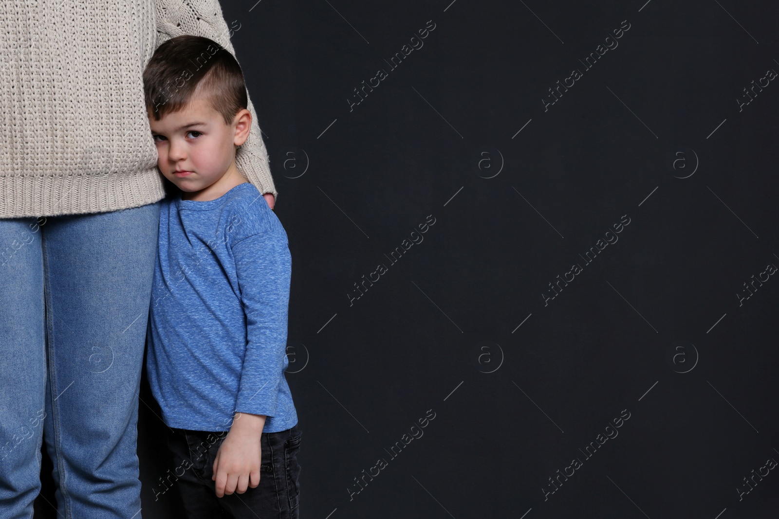 Photo of Sad little boy hugging his mother on black background, space for text