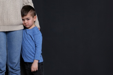 Sad little boy hugging his mother on black background, space for text