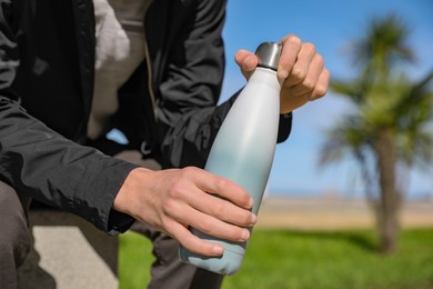 Photo of Man holding thermo bottle in park on sunny day, closeup
