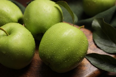 Photo of Ripe green apples with leaves and water drops on wooden board, closeup