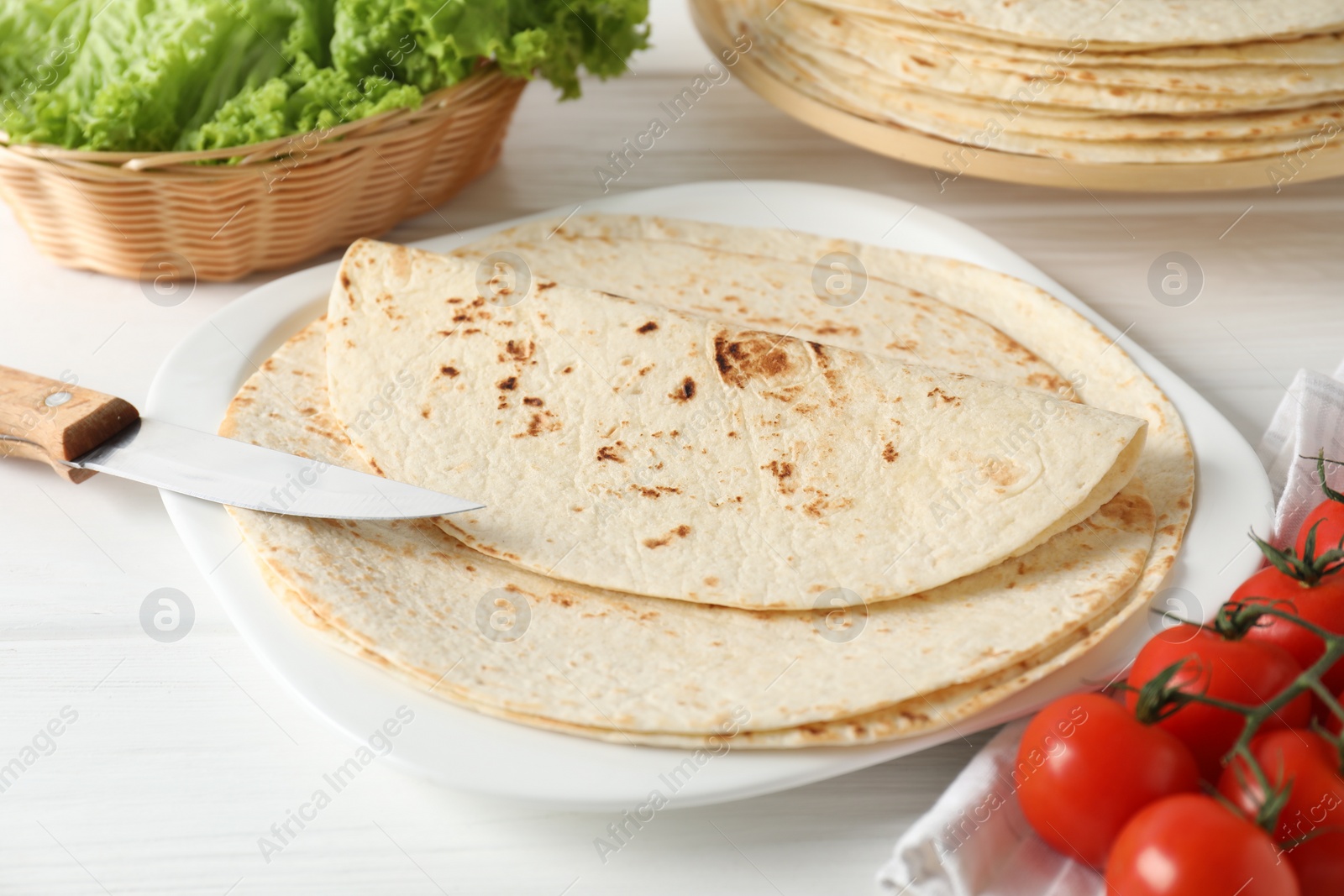 Photo of Tasty homemade tortillas, tomatoes, lettuce and knife on white wooden table