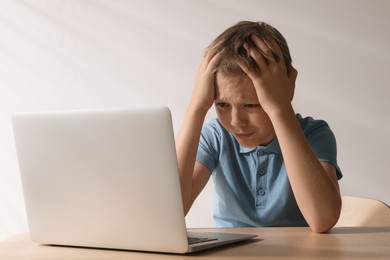 Photo of Upset boy with laptop at wooden table. Cyber bullying