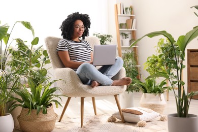 Photo of Relaxing atmosphere. Woman with laptop sitting on armchair surrounded by houseplants at home