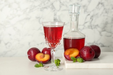 Photo of Delicious plum liquor, mint and ripe fruits on white table. Homemade strong alcoholic beverage