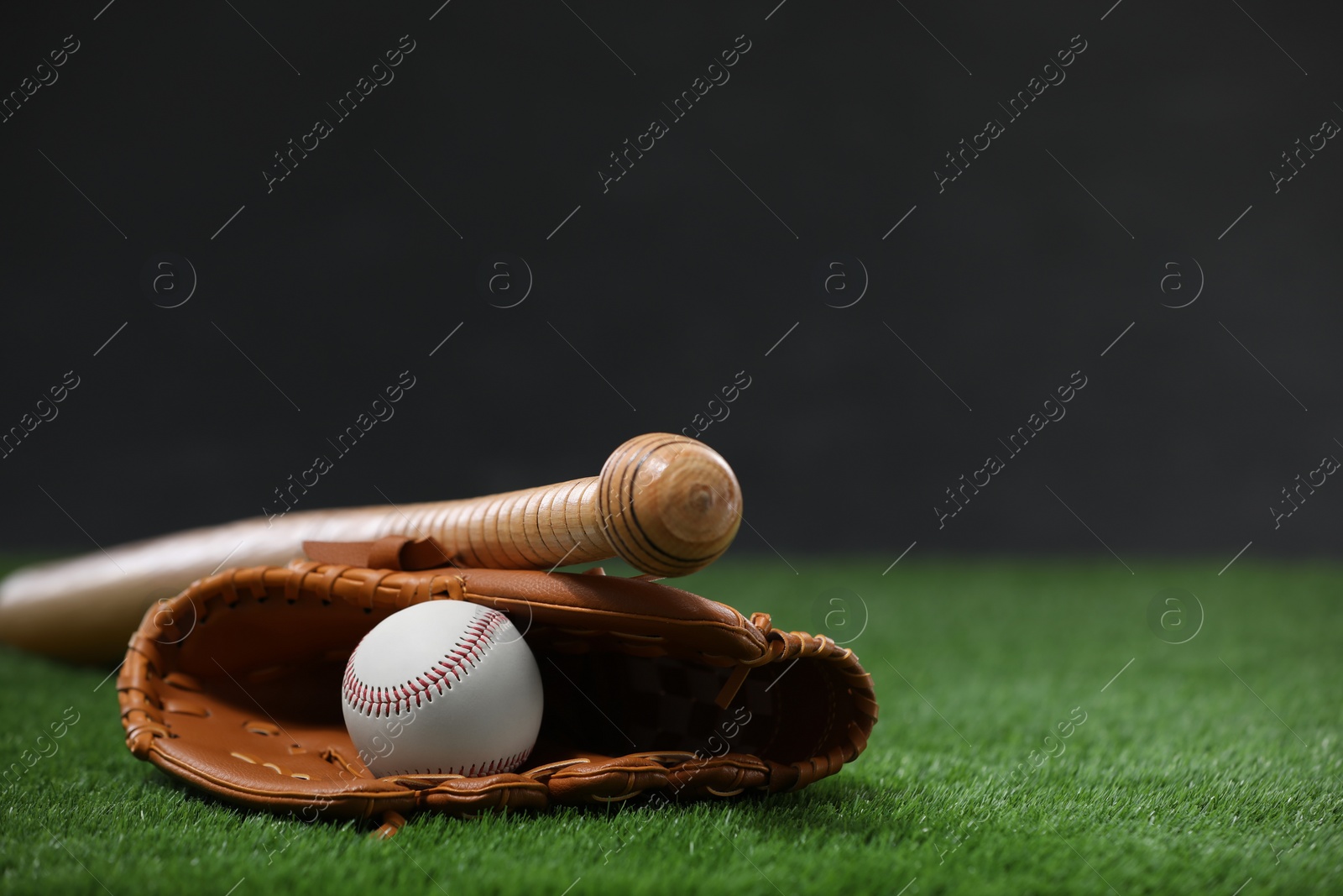 Photo of Baseball bat, leather glove and ball on green grass against dark background. Space for text