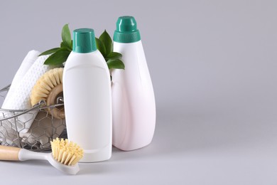 Photo of Bottles of cleaning product, brushes, rags and green leaves on light background. Space for text