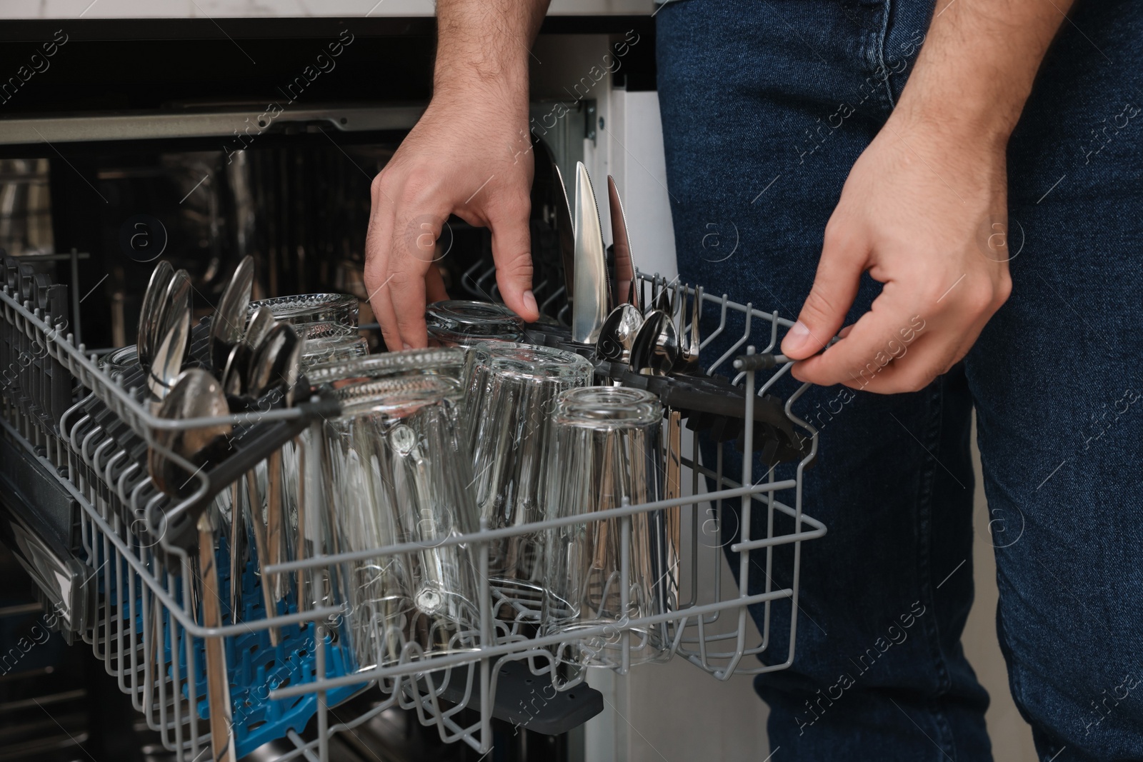 Photo of Man loading dishwasher with glass and cutlery indoors, closeup