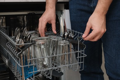 Man loading dishwasher with glass and cutlery indoors, closeup