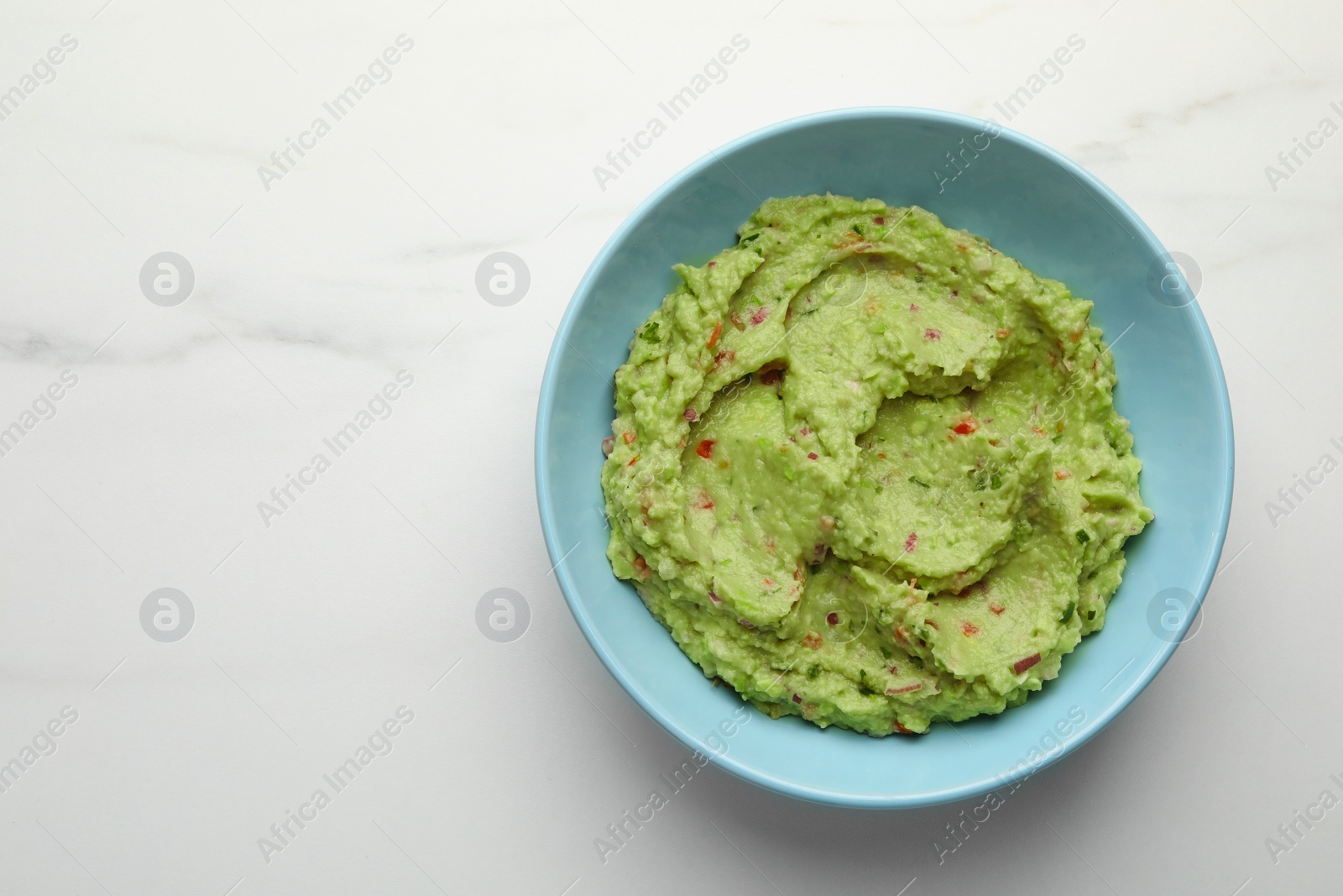 Photo of Bowl with delicious fresh guacamole on white marble table, top view. Space for text