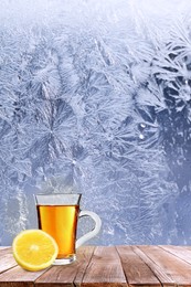 Image of Cup of hot tea on wooden table near window covered with frost 