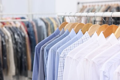 Photo of Dry-cleaning service. Many different clothes hanging on rack indoors, closeup