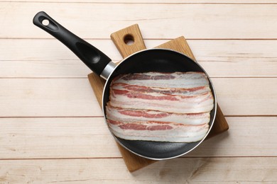 Photo of Slices of raw bacon in frying pan on wooden table, top view