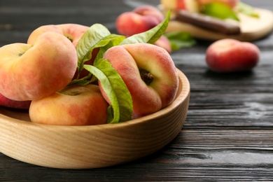 Photo of Fresh ripe donut peaches on black wooden table, closeup
